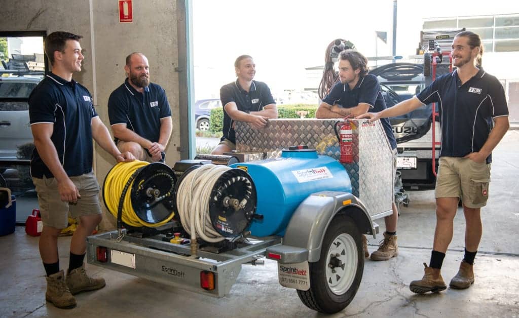 A team of five smiling plumbers from Tubeline Plumbing preparing to leave their warehouse